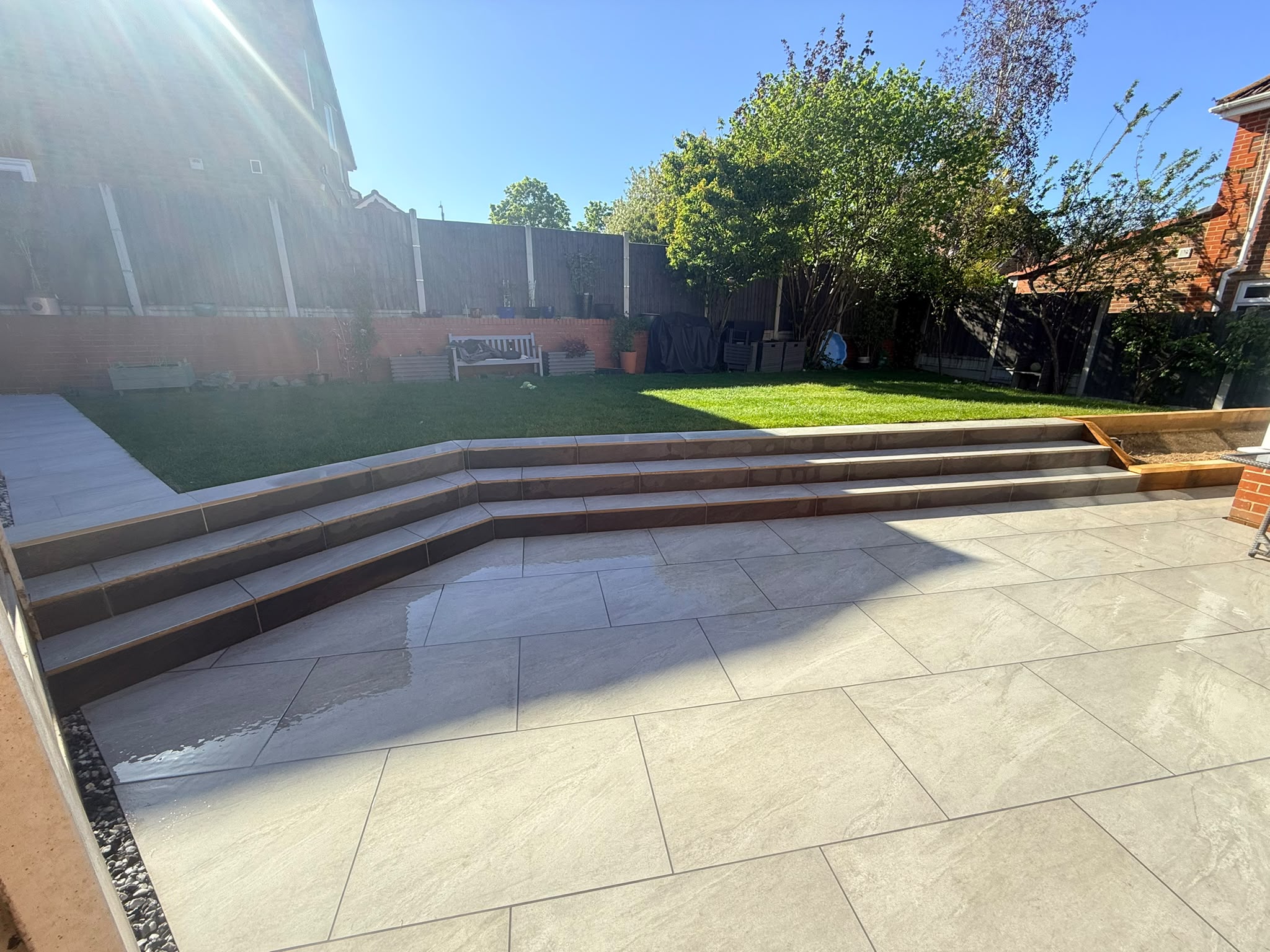 After: Multi-level porcelain patio with wide modern steps and neat lawn in Chelmsford