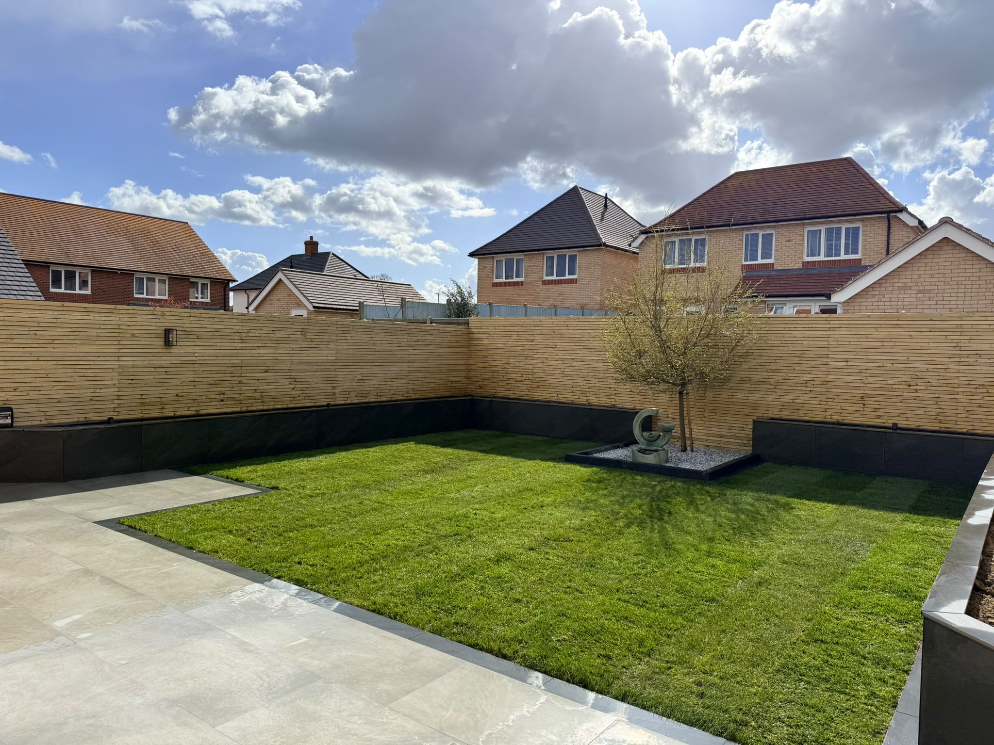 Neat lawn framed by porcelain paving and slatted fencing on the Redrow estate, Witham